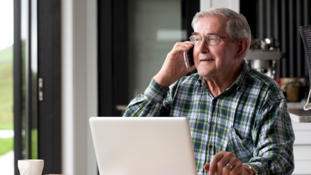 Older man talking on phone in front of computer