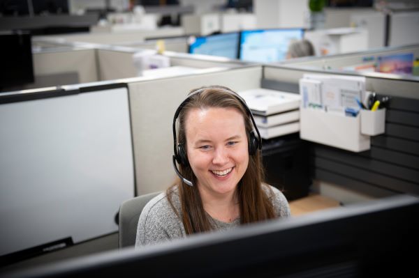 Photo of a person wearing a headset looking at a computer and smiling.