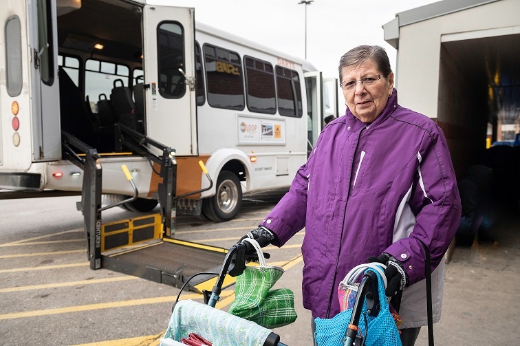 Photo of a person with a walker standing in front of a bus with a wheelchair lift.