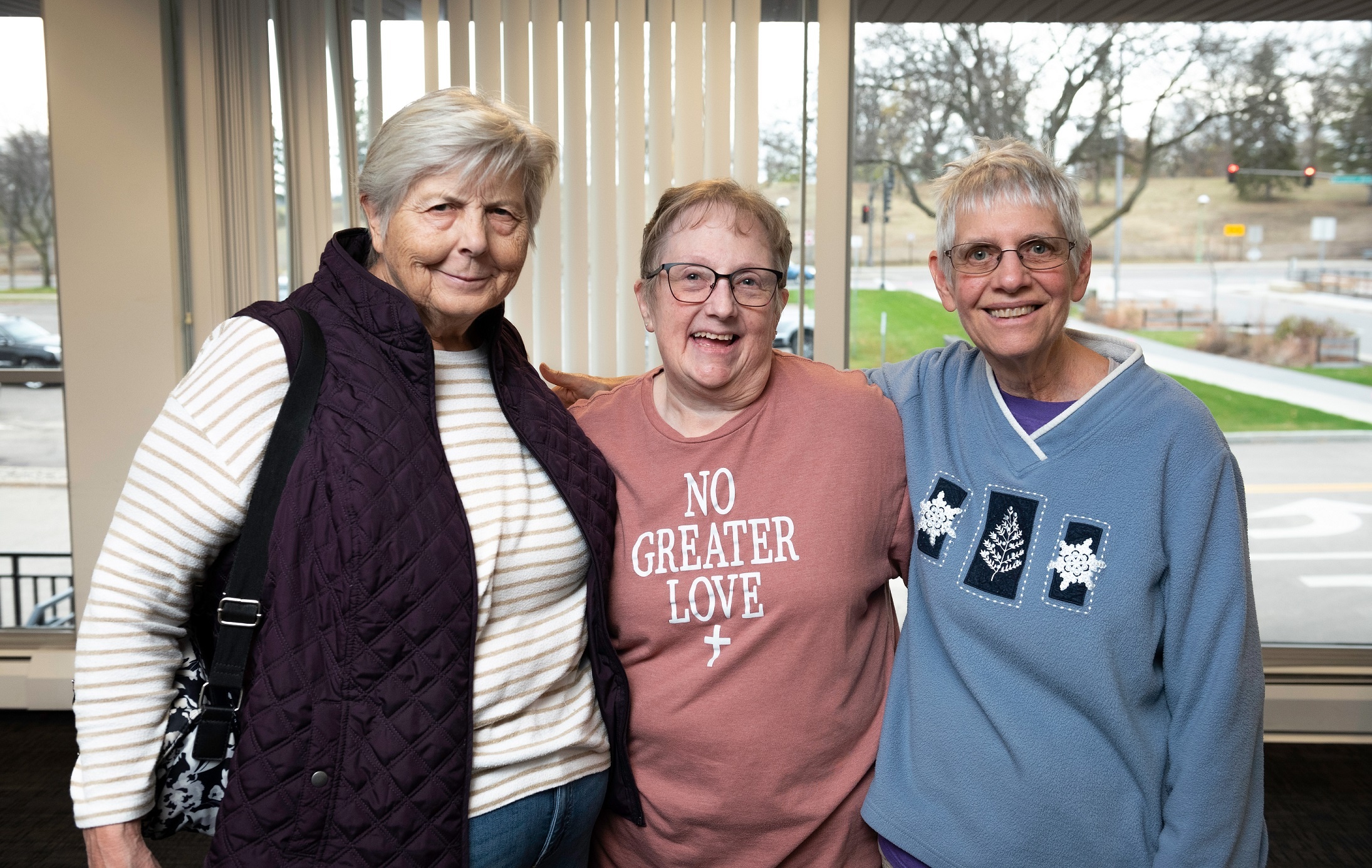 Three smiling senior women facing camera with arms embracing.