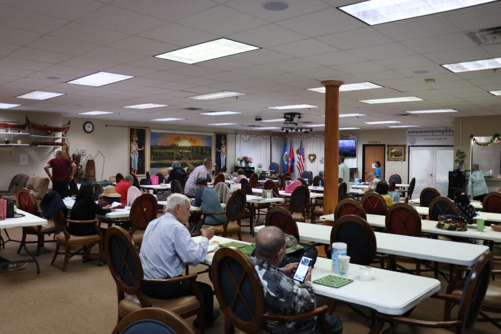 Photo of a large room with several people seated at tables.