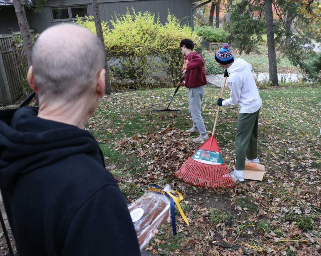 Photo of two people raking as another person looks on.