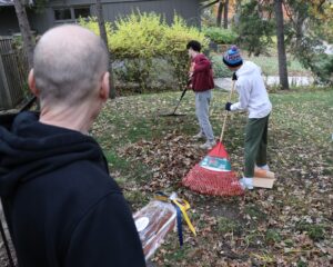 Photo of two people raking as another person looks on.